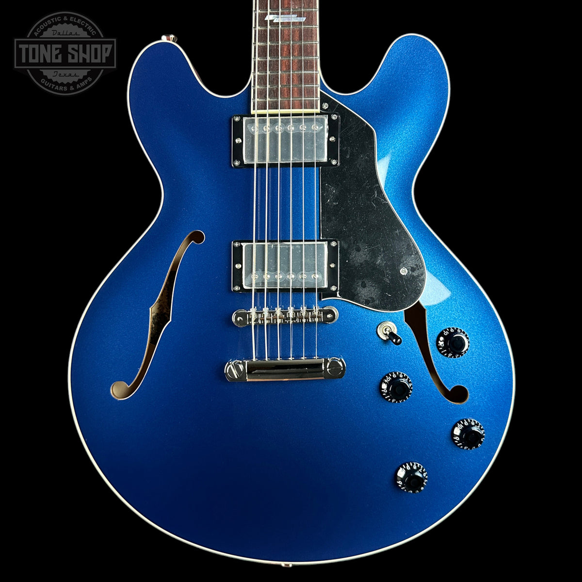 Blue electric guitar with a black pickguard on a black background, featuring the Tone Shop logo.