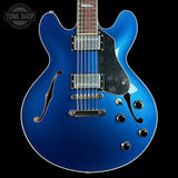 Blue electric guitar with a black pickguard on a black background, featuring the Tone Shop logo.