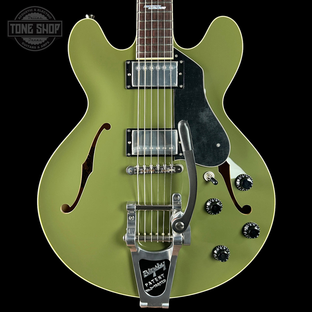 Green electric guitar with a black pickguard on a black background, featuring the Tone Shop logo.