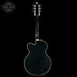 Back view of a black electric guitar on a black background with 'Tone Shop' logo.
