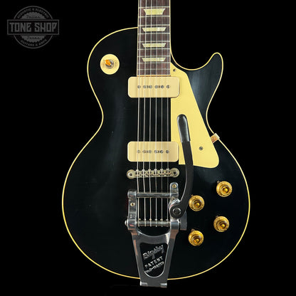 Black electric guitar with gold hardware on a black background, featuring 'Tone Shop' logo.