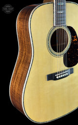 Close-up of an acoustic guitar body showing the natural wood top, sound hole rosette, side bout, and part of the dark fretboard against a black background.