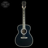 A black acoustic guitar with white binding and gold hardware, displayed vertically against a solid black background. A circular 'TONE SHOP' watermark is visible in the top-left corner.