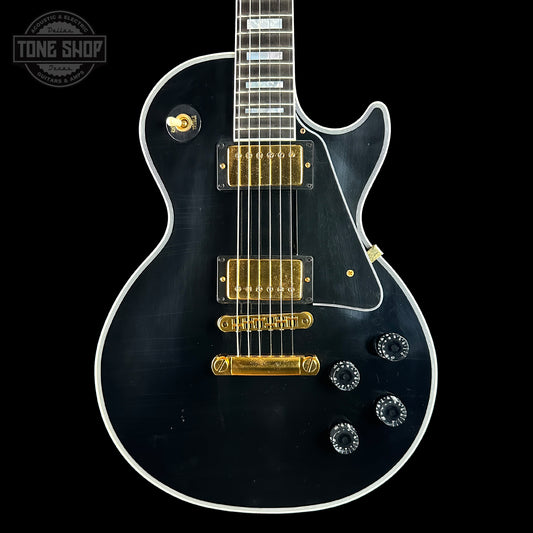 Black electric guitar with gold hardware on a black background, featuring 'Tone Shop' logo.
