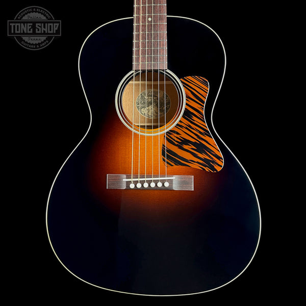 A close-up studio shot of an acoustic guitar body against a black background, showing a dark blue to brown sunburst finish, white binding, a tiger-stripe style pickguard, and a silver bridge. A Tone Shop watermark is visible in the top left corner.