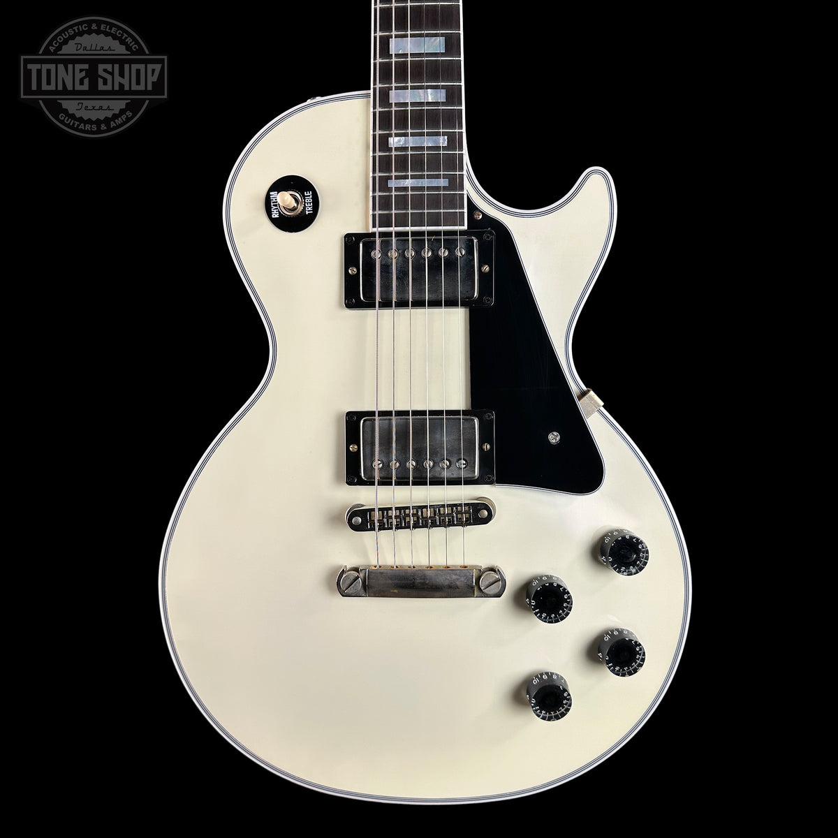White electric guitar with black details on a black background, featuring 'Tone Shop' branding.