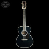A black acoustic guitar with white binding and a dark pickguard, shown vertically against a solid black background. A circular 'TONE SHOP' watermark is visible in the top-left corner.