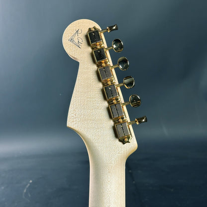 Close-up of a guitar headstock with tuning pegs on a dark blue background