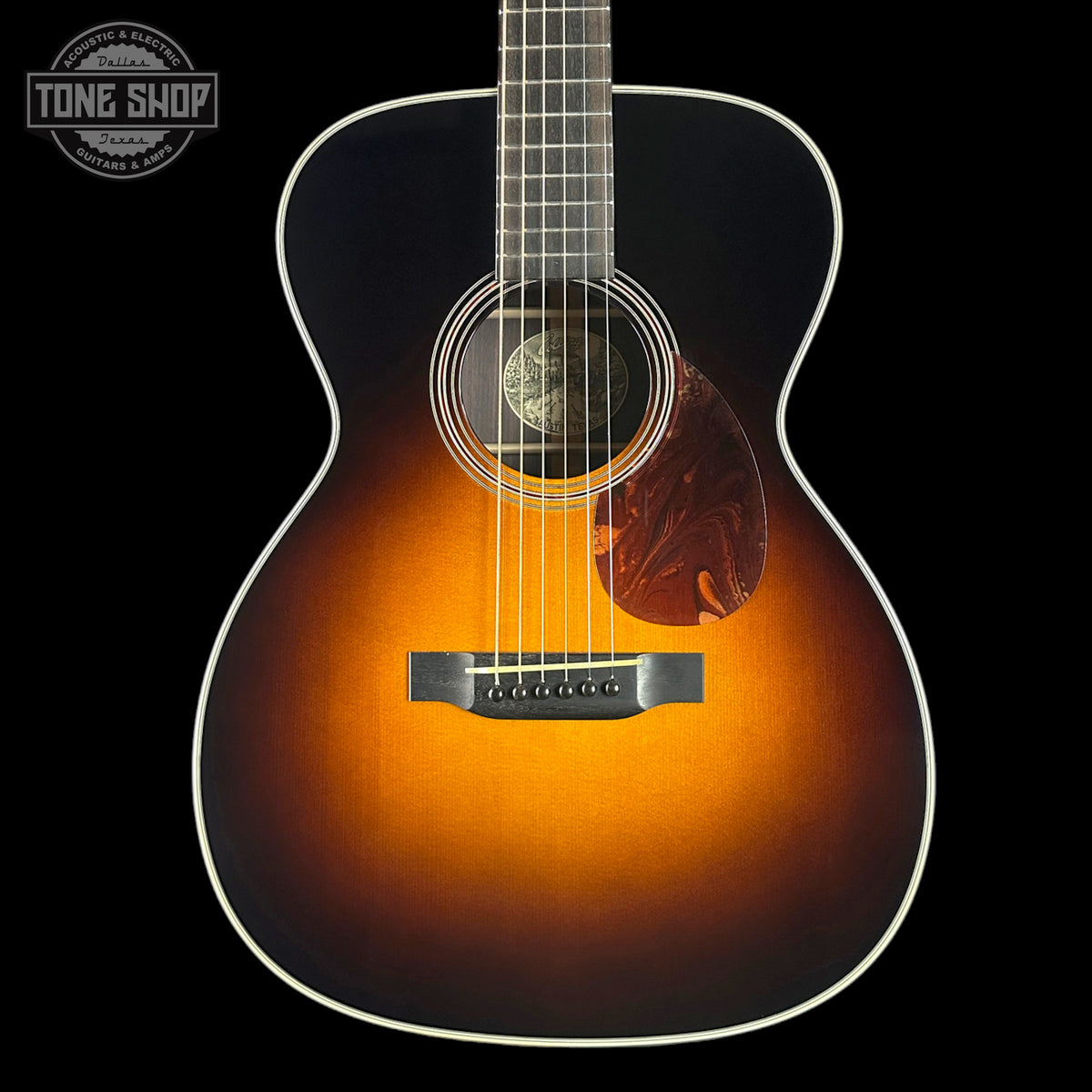 Acoustic guitar with a sunburst finish on a black background, featuring the Tone Shop logo.