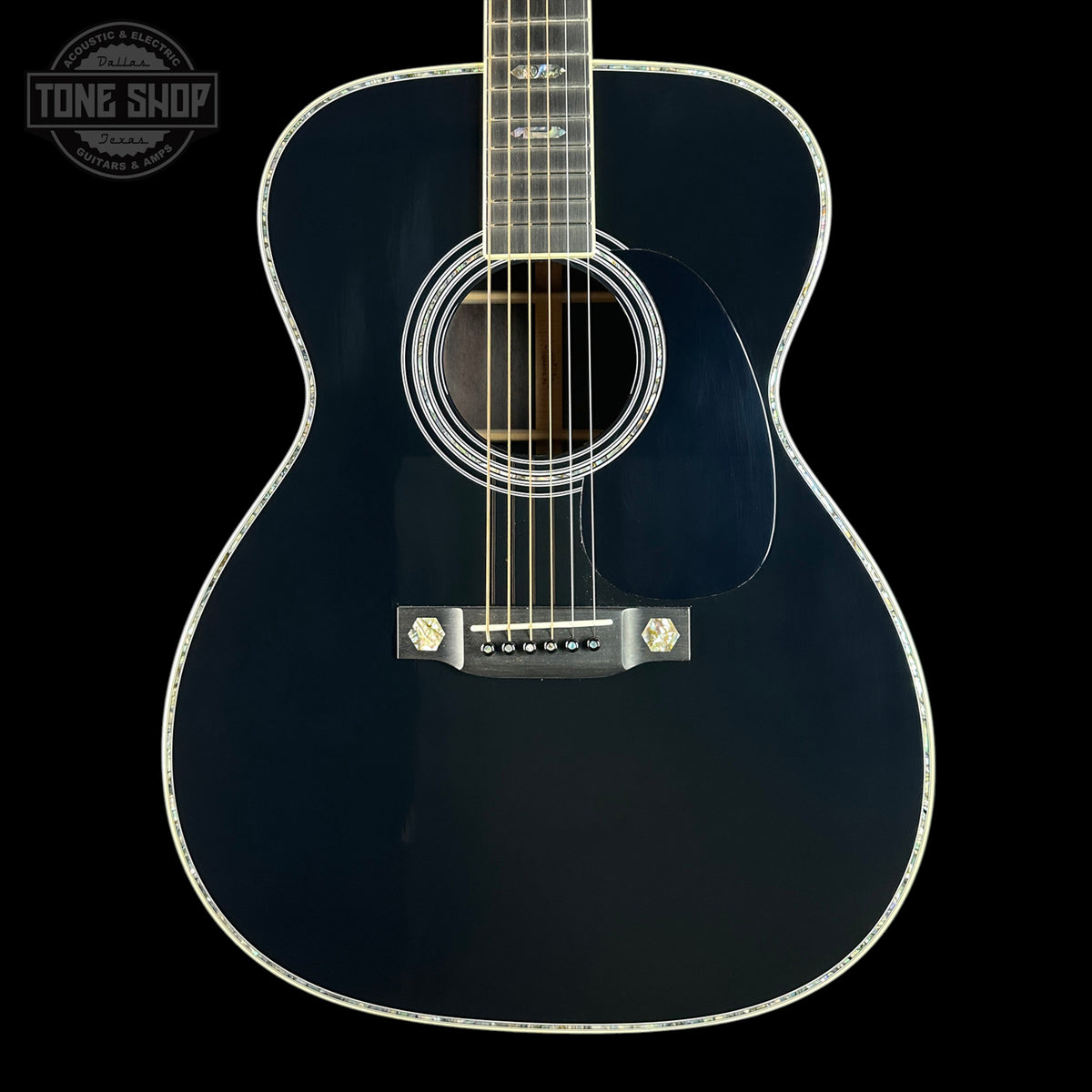 A close-up studio shot of a dark navy blue acoustic guitar against a solid black background, featuring a glossy finish, white rosette detailing, and a silver bridge.