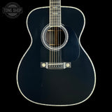 A close-up studio shot of a dark navy blue acoustic guitar against a solid black background, featuring a glossy finish, white rosette detailing, and a silver bridge.