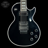 A black electric guitar with chrome hardware and white binding, shown from the front against a black background. A Tone Shop watermark is visible in the top-left corner.