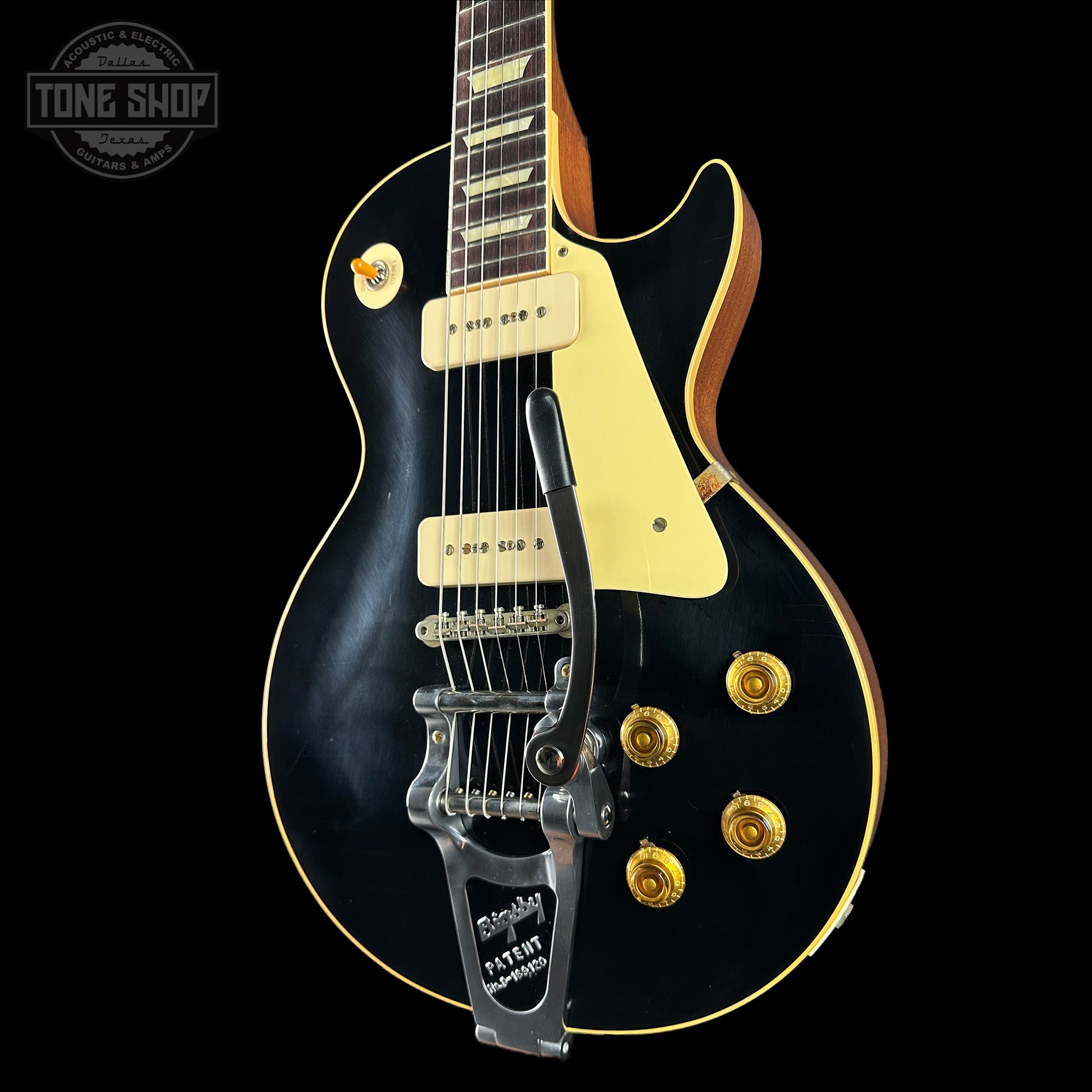 Black electric guitar with gold hardware on a black background, featuring 'Tone Shop' logo.