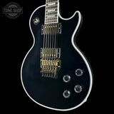Black electric guitar with white pickguard on a black background, featuring 'Tone Shop' logo.