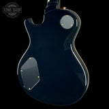 The rear view of a glossy black electric guitar body, featuring a circular silver control plate and a larger rectangular silver plate with gold-tone screws, set against a solid black background.