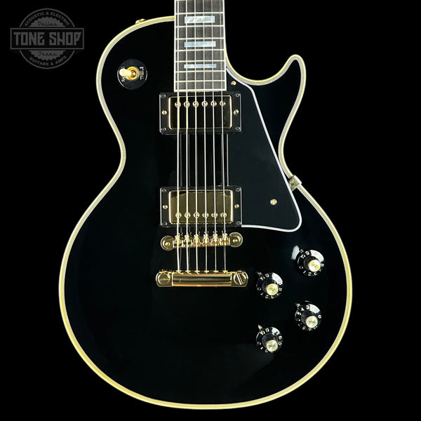 Black electric guitar with gold hardware on a black background, featuring 'Tone Shop' logo.