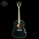 A dark green acoustic guitar with gold hardware and a striped pickguard, shown vertically against a solid black background. A Tone Shop watermark is visible in the top-left corner.