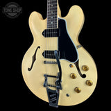 A cream-colored electric guitar with a black pickguard, black pickups, gold hardware, and a black bridge, shown against a solid black background. A Tone Shop watermark is visible in the top left corner.
