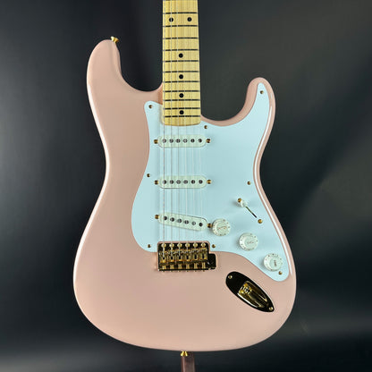 Pink electric guitar with a light blue pickguard on a dark background