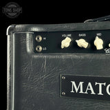 Close-up of a black textured amplifier cabinet with cream control knobs labeled VOLUME, BASS, and MID, plus a black nameplate with white lettering. A Tone Shop watermark appears in the top-left corner.