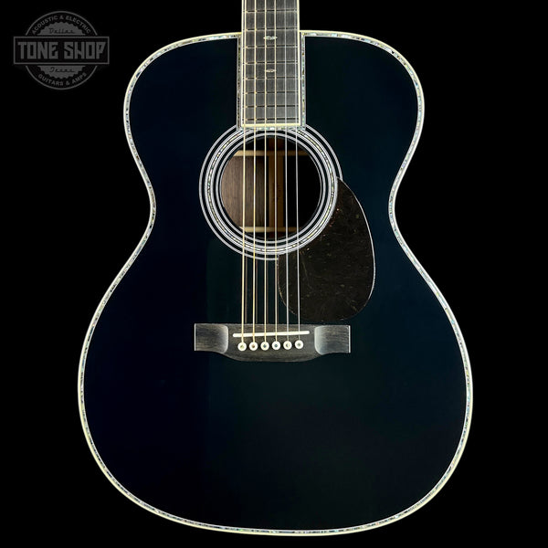 A close-up studio shot of an acoustic guitar body against a black background, showing a glossy dark blue finish, white rosette, pickguard, and binding, with six strings visible. A Tone Shop logo watermark is in the top-left corner.