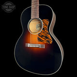 A close-up of an acoustic guitar body against a black background, featuring a dark brown sunburst finish, a tiger-stripe style pickguard, and a natural wood soundboard. A Tone Shop watermark is visible in the top-left corner.