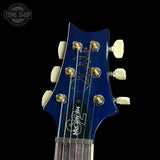 Close-up of a blue electric guitar headstock with brand logo on a black background