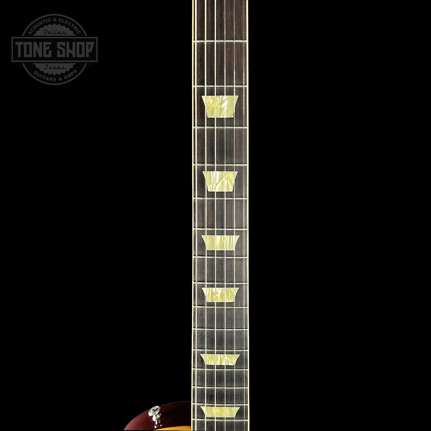 Close-up of a guitar neck with frets on a black background, featuring the Tone Shop logo.