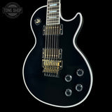 Black electric guitar with a white pickguard on a black background, featuring the Tone Shop logo.