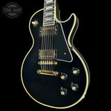 Black electric guitar with gold hardware on a black background, featuring 'Tone Shop' logo.