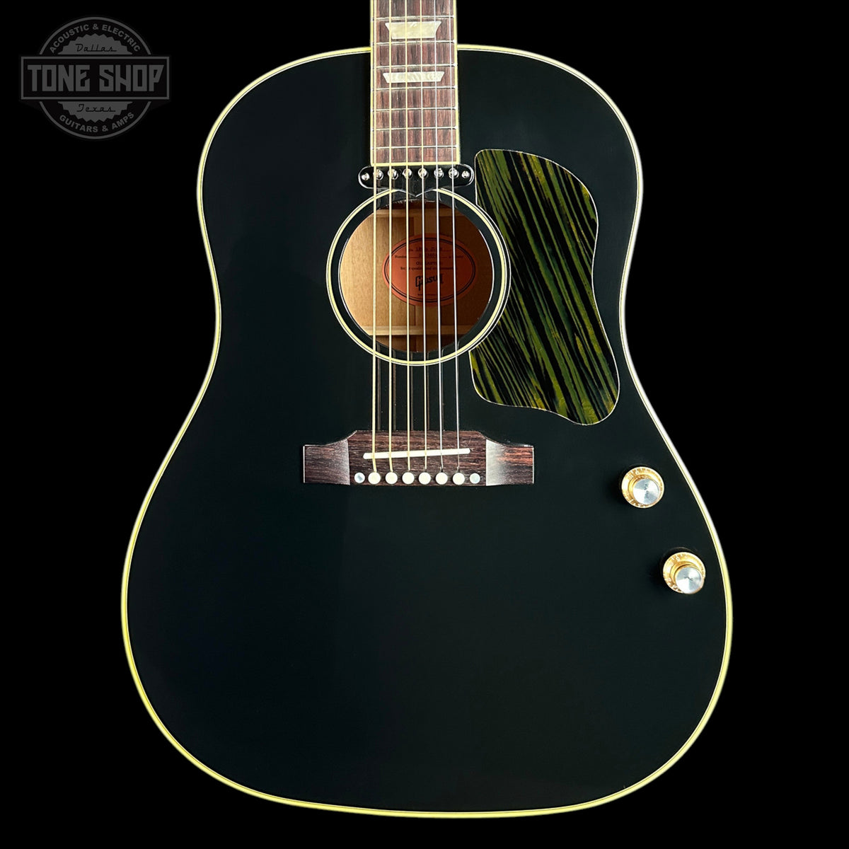 A close-up of a black acoustic guitar body with gold-toned binding, a green-and-black striped pickguard, and gold control knobs on a black background. A Tone Shop watermark is visible in the upper left corner.