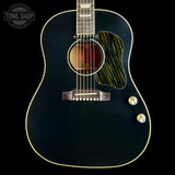 A close-up studio shot of an acoustic guitar body against a black background, featuring a glossy black finish, gold-toned binding, a green and black striped pickguard, and two gold control knobs.