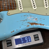 A close-up of a light blue electric guitar body with distressed brown paint, resting on a digital scale showing 7.91 lbs.