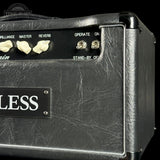 Close-up of a black guitar amplifier cabinet with textured leather-like front panel, cream control knobs, and a black nameplate reading "BLESS" on a black background.