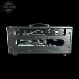 The rear view of a black textured metal Marshall amplifier head against a solid black background, showing the input jacks, fuse socket, and speaker terminals.