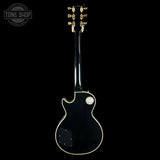 Black electric guitar with gold hardware on a black background, featuring 'Tone Shop' logo.