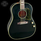 A close-up of a black acoustic guitar body with gold-toned hardware, a decorative pickguard, and cream-colored binding, shown against a black background with a Tone Shop watermark in the upper left.