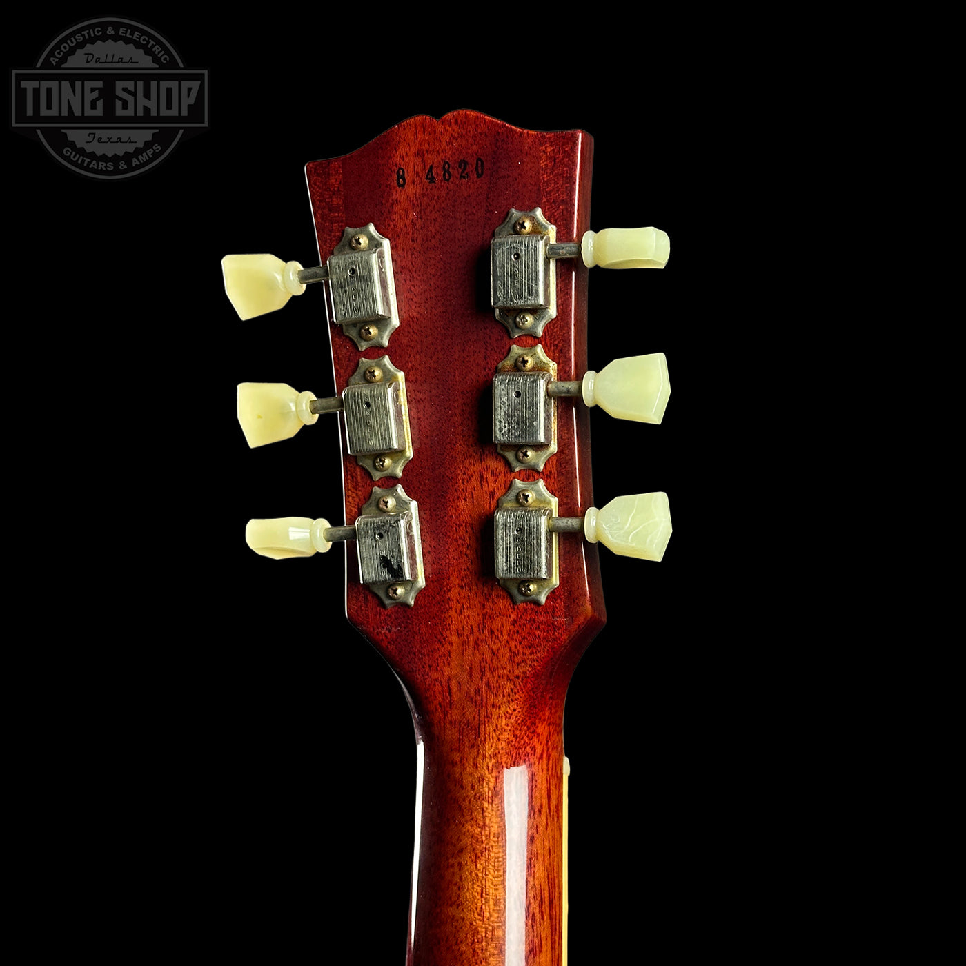 Close-up of a guitar headstock with tuning pegs on a black background, featuring the Tone Shop logo.
