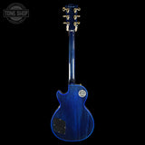 A blue Gibson Les Paul Custom electric guitar shown from the back, featuring a glossy blue finish, gold hardware, and a black pickguard, set against a solid black background with a Tone Shop watermark in the top left corner.
