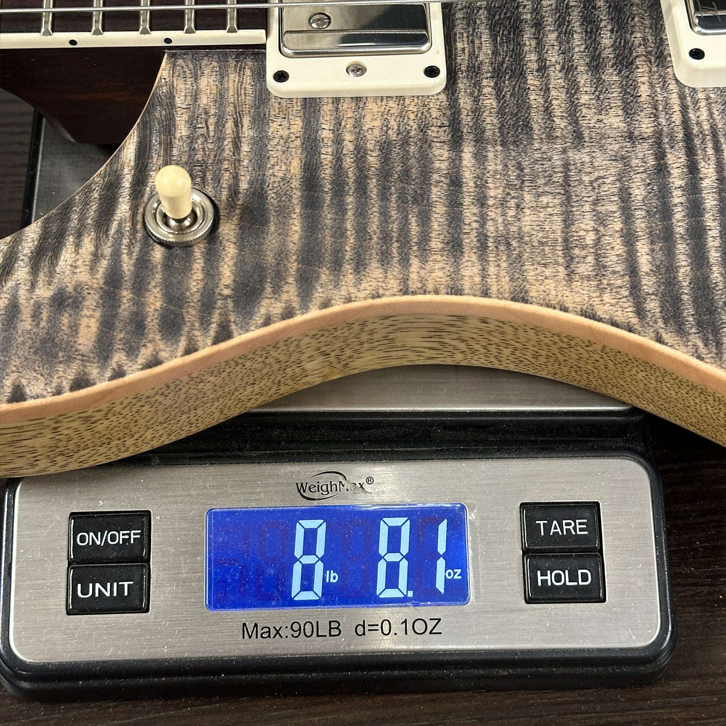 Digital scale displaying weight of a guitar, with a close-up view of the scale and guitar.