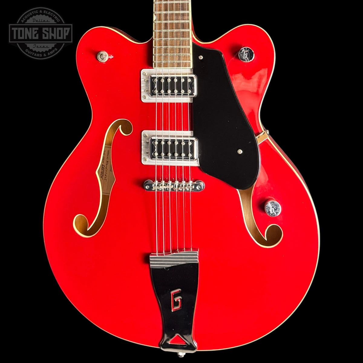 Red electric guitar with a black pickguard on a black background, featuring the Tone Shop logo.