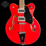 Red electric guitar with a black pickguard on a black background, featuring the Tone Shop logo.