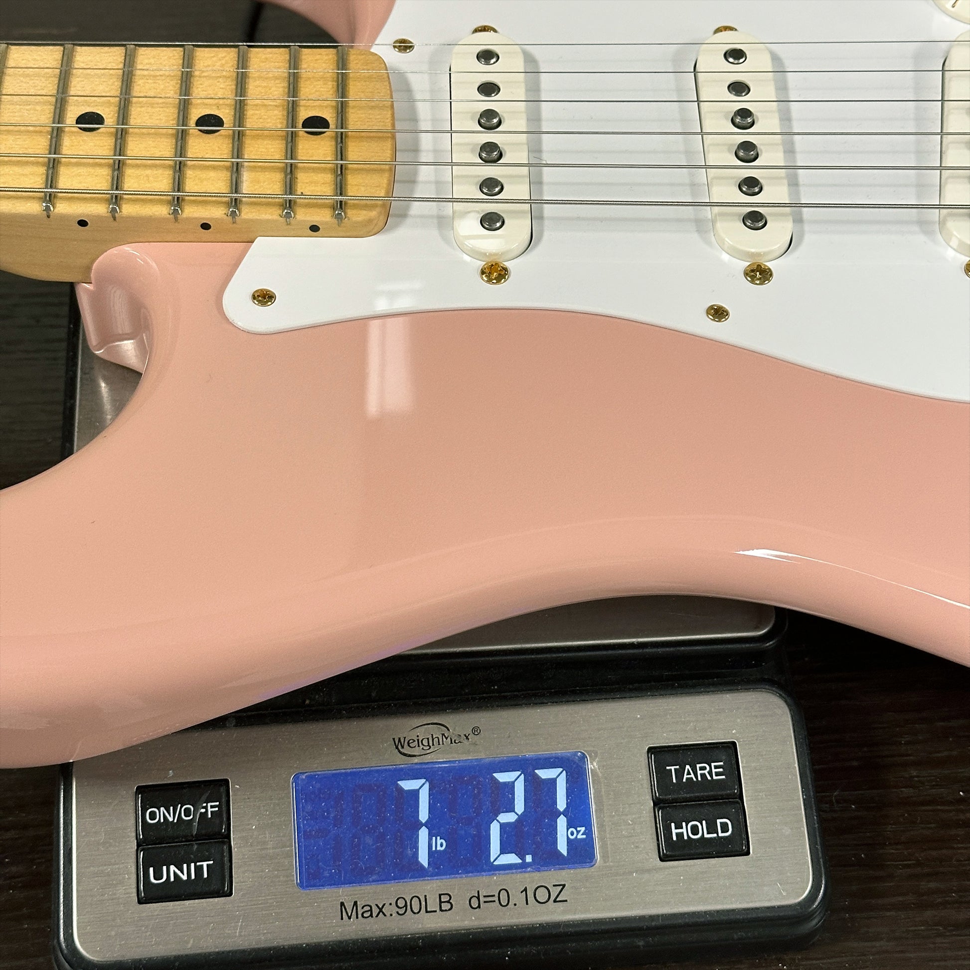 Pink electric guitar on a digital scale displaying weight