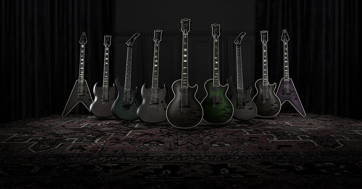 Group of multiple dark finished epiphone electric guitars against a dark background.