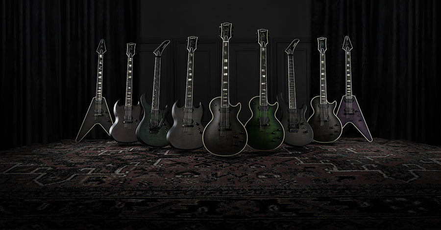 Group of multiple dark finished epiphone electric guitars against a dark background.