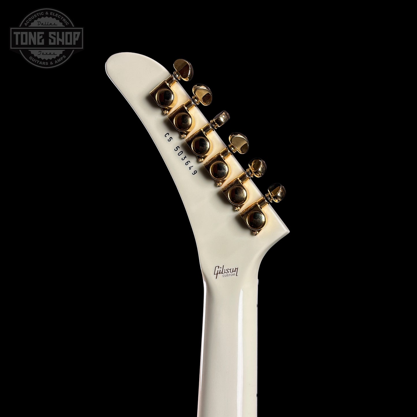 Close-up of a white guitar neck with gold tuning pegs on a black background, featuring the Gibson logo.