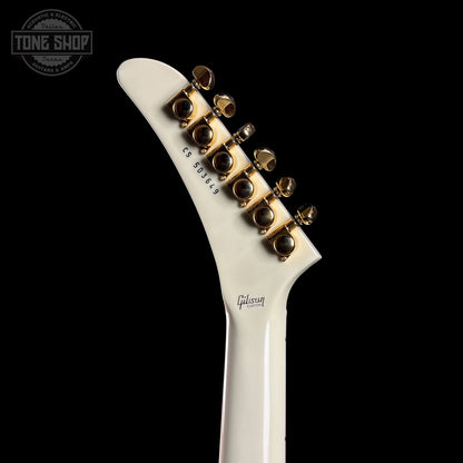 Close-up of a white guitar neck with gold tuning pegs on a black background, featuring the Gibson logo.