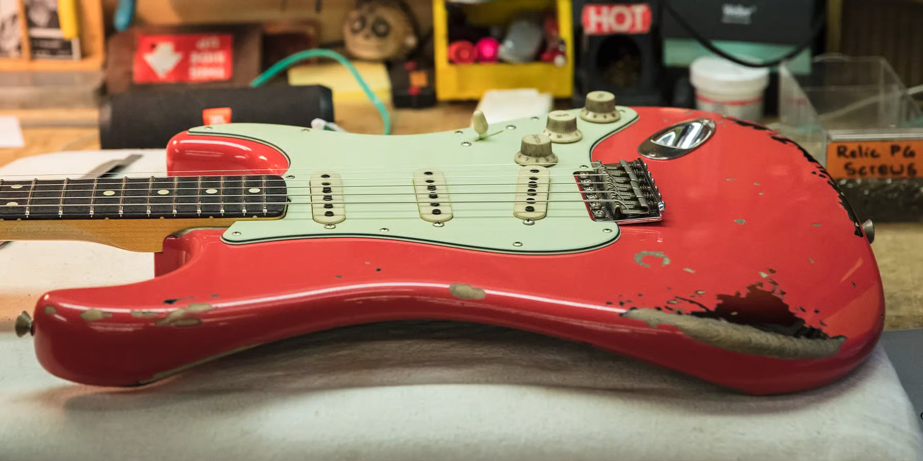 Red worn electric strat guitar on a workbench.