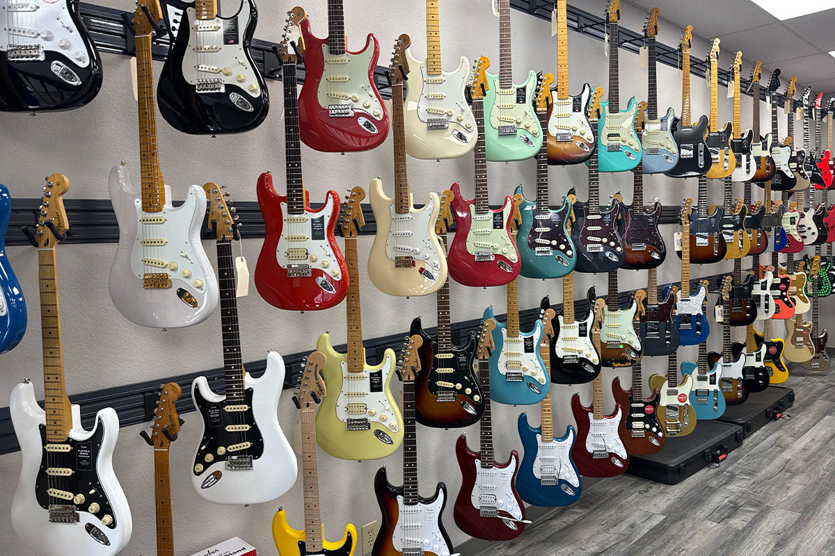 Wall of electric guitars in multiple colors on hooks against a white wall.
