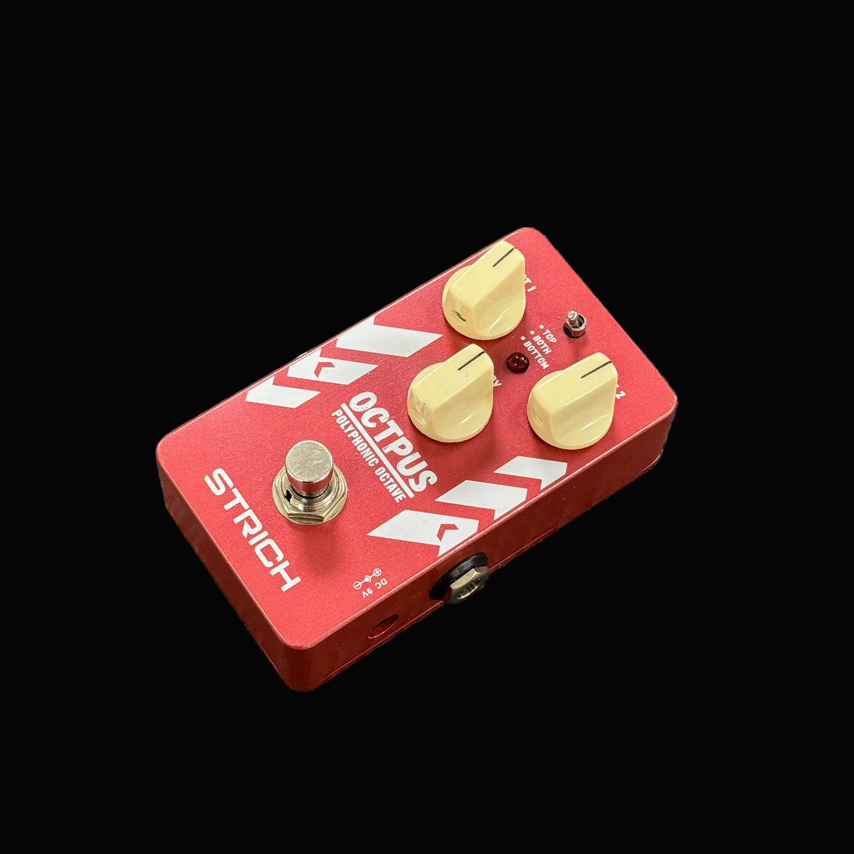 Red guitar effects pedal with gold knobs on a textured surface